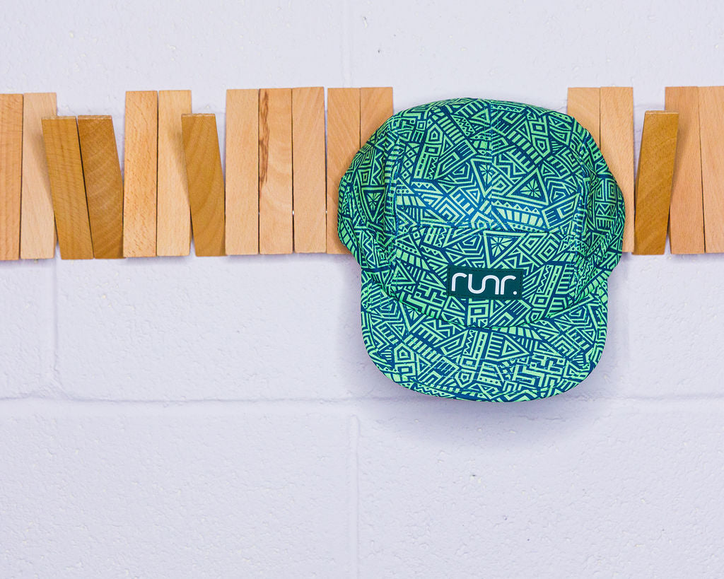 Green patterned cap with 'run' logo on a wooden block background
